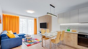 Ein modernes Wohnzimmer mit einem blauen Sofa, einem farbenfrohen Teppich und einem Essbereich mit Tisch für vier Personen.