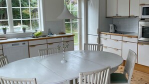 Eine moderne Küche mit weißen Schränken, einer zentralen Kochinsel und einem Essbereich mit rundem Tisch und Stühlen.