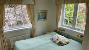 Ein Schlafzimmer mit einem Bett, zwei Vorhängen, einem Heizkörper und einem gerahmten Bild an der Wand.