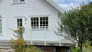 Ein weißes, zweistöckiges Haus mit geneigtem Dach, einer Veranda und einem kleinen Baum im Vorgarten.