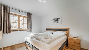 Een slaapkamer met een bed, nachtkastje, raam met gordijnen en een wandlamp.