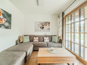 A modern living room with a sectional sofa, a wooden coffee table, and large windows. - Dachstein West 1b by Interhome (Rußbach am Pass Gschütt)