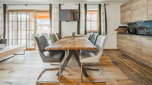 Een moderne keuken met een houten eettafel, grijs gestoffeerde stoelen en een inbouwfornuis.
