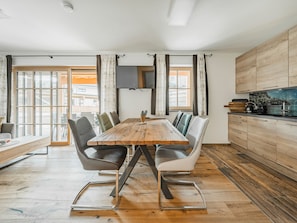 A modern kitchen with a wooden dining table, grey upholstered chairs, and a built-in stove. - Dachstein West 1b by Interhome (Rußbach am Pass Gschütt)