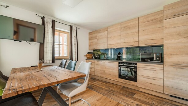 Een moderne keuken met houten kastjes, een ingebouwde magnetron, en een eethoek met een houten tafel en stoelen.