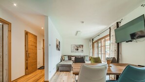 Een moderne woonkamer met houten vloer, een zithoek, een eettafel en een tv aan de muur.