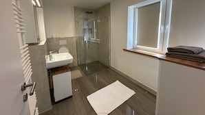 A modern bathroom with a glass shower enclosure, a white sink, and a window with a towel rack. - Luxus Apratment by Interhome (Leipzig)