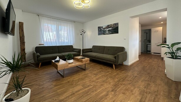 A modern living room with two sofas, a coffee table, and a floor lamp. There is a painting on the wall and a television mounted on the wall. - Luxus Apratment by Interhome (Leipzig)