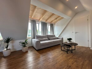 Een moderne loft slaapkamer met een schuine hemel, een grijze bank, houten vloeren en twee potplanten.