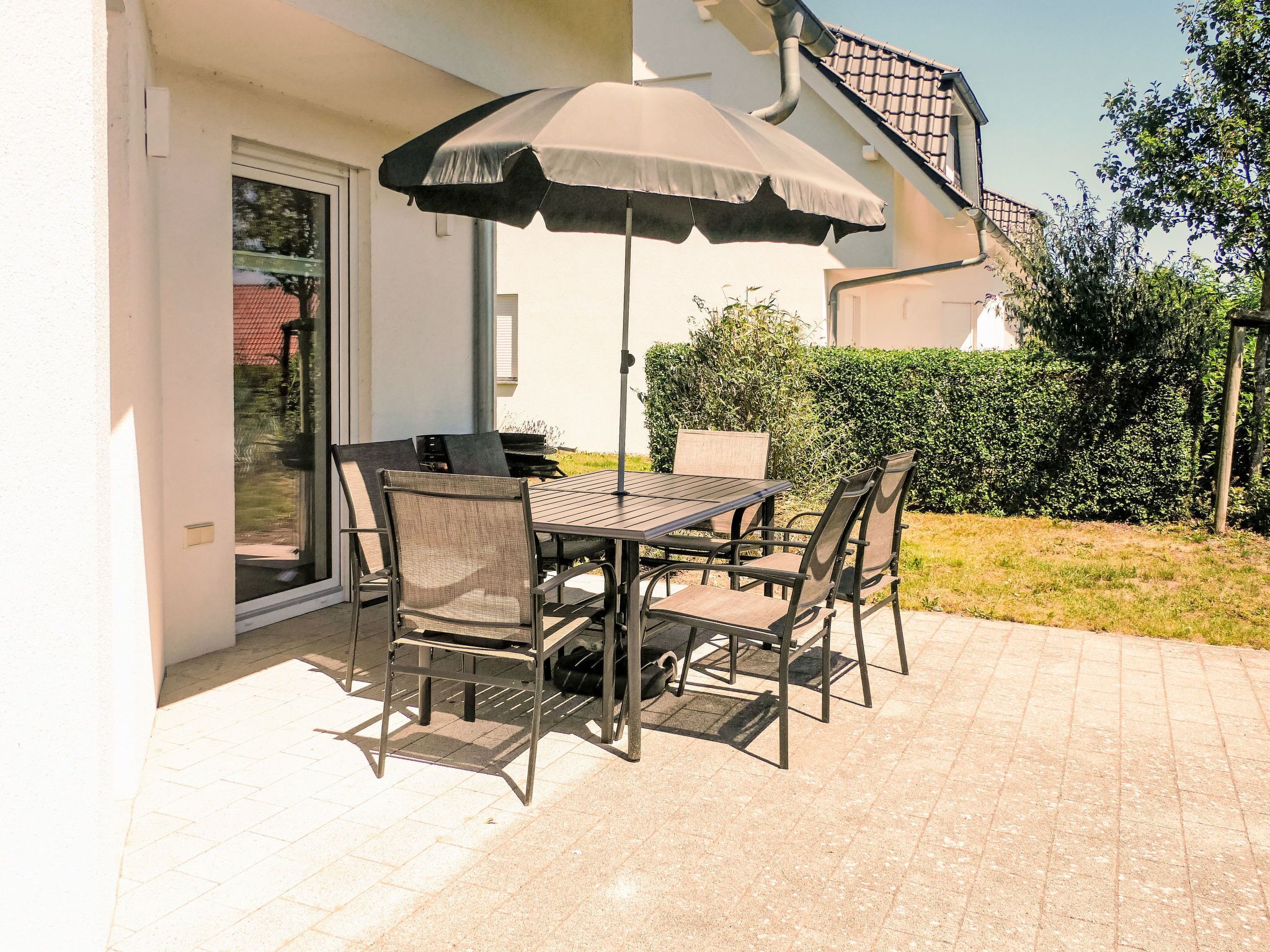 An outdoor patio with a table and chairs, a grill, and a covered umbrella.