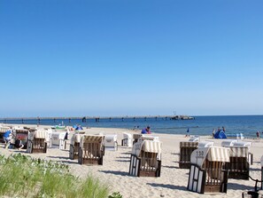 A beach with rows of numbered beach chairs and umbrellas, a pier in the background, and a clear blue sky. - Vacation home  by Interhome (Bansin)