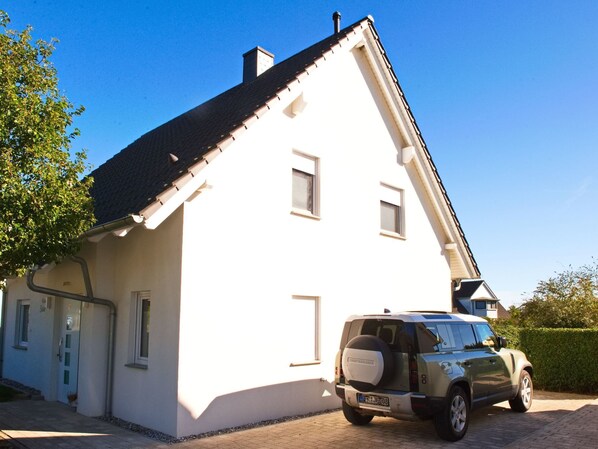 A white building with a black roof, a driveway, and a parked SUV. - Vacation home  by Interhome (Bansin)