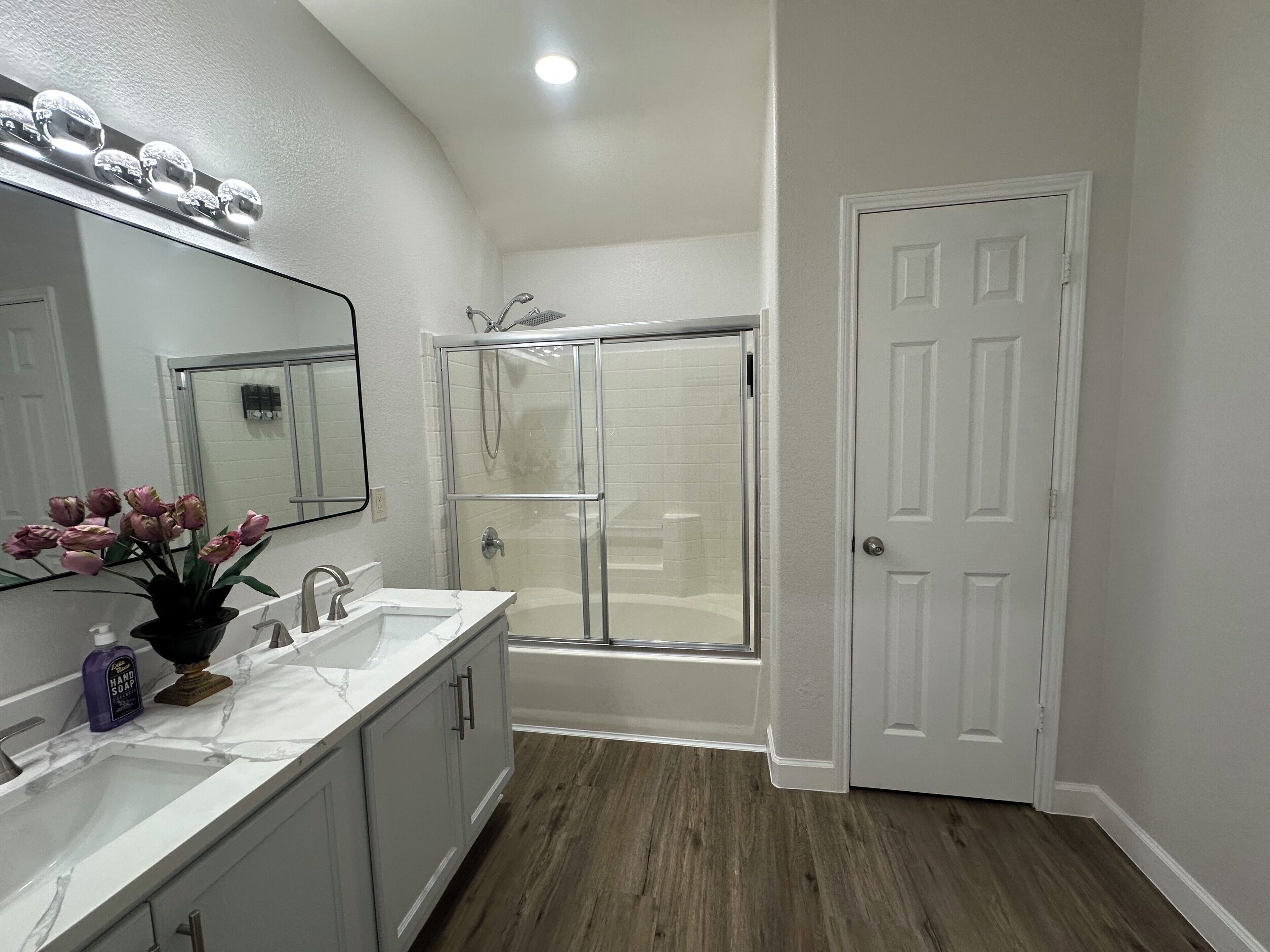 Un bagno con doccia vetrata, un lavandino con piano in marmo e una porta con stipite bianco.