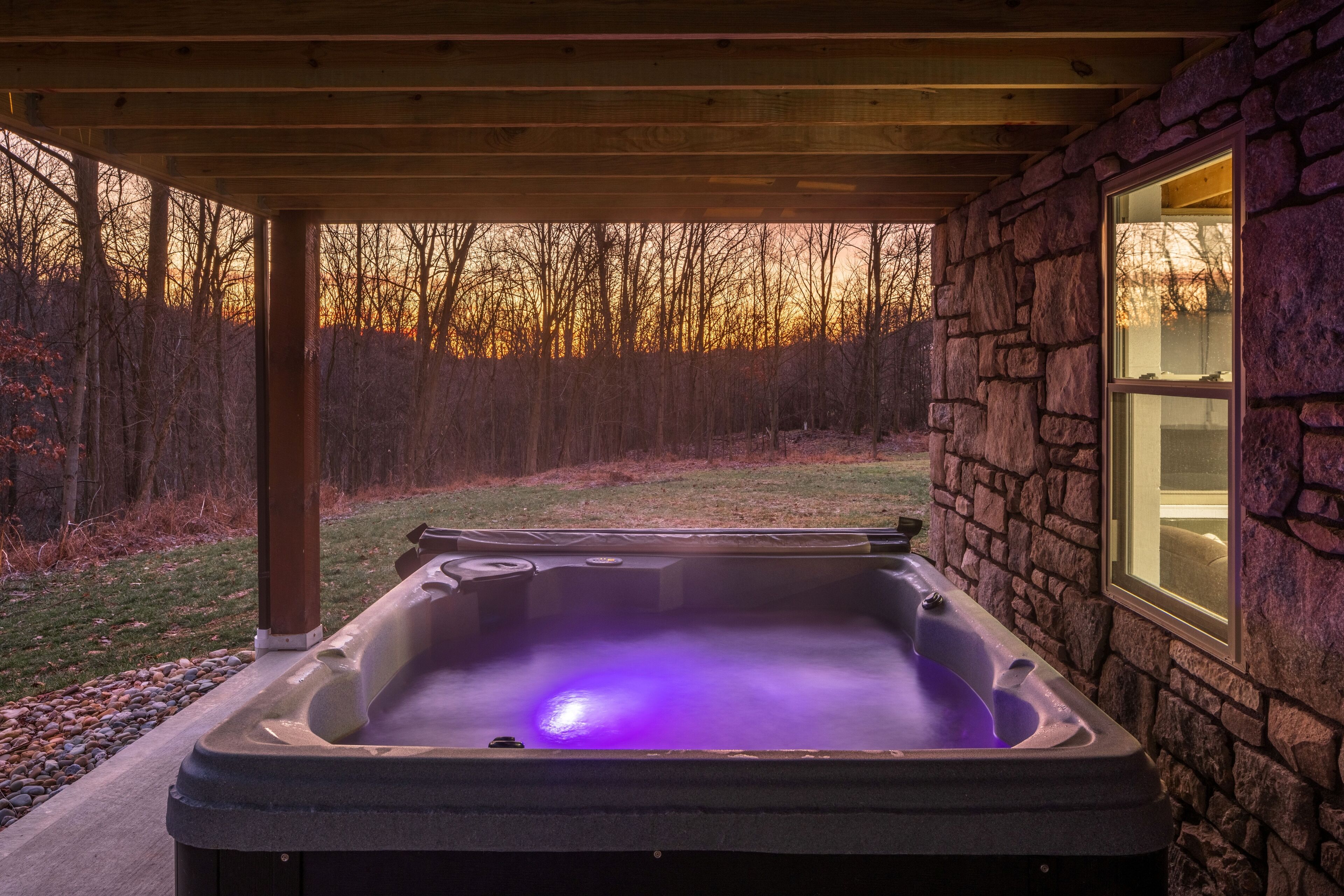 Een hottub onder een houten pergola met een stenen muur en een raam.