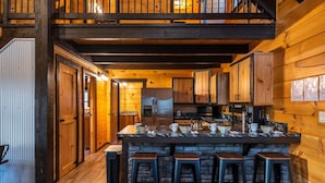 A kitchen with wooden walls, a central island with stools, and a refrigerator. - Schilling Hill (New Philadelphia)