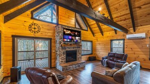 A log cabin interior with a stone fireplace, leather sofas, wooden floors, and a large TV screen. - Schilling Hill (New Philadelphia)