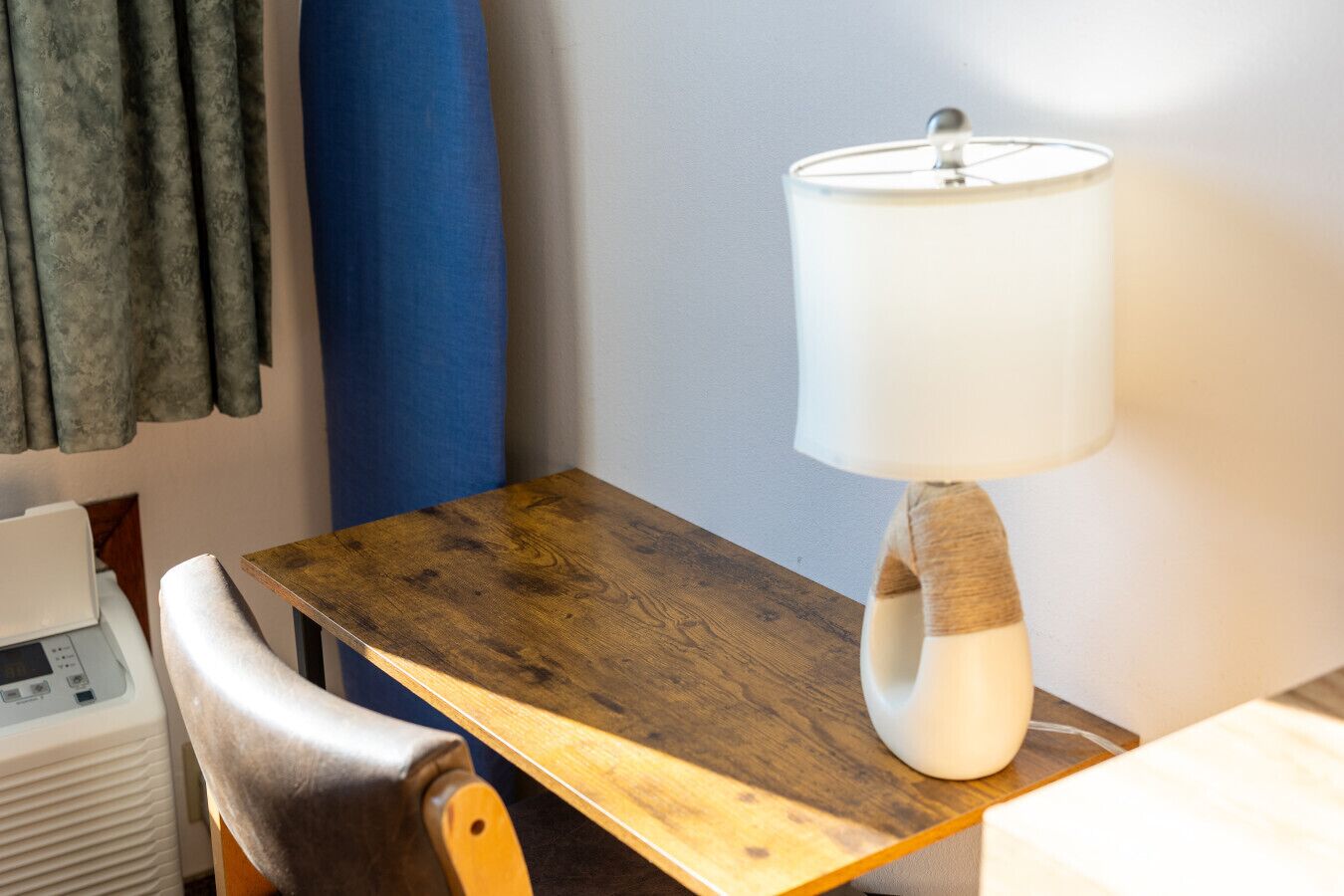 Una mesa de madera con una lámpara, una silla y un dispositivo blanco a la izquierda.