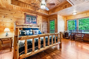 Ein Holzblockhaus-Interieur mit einem Bett, einem Schreibtisch und einem Fenster mit Blick auf Bäume.