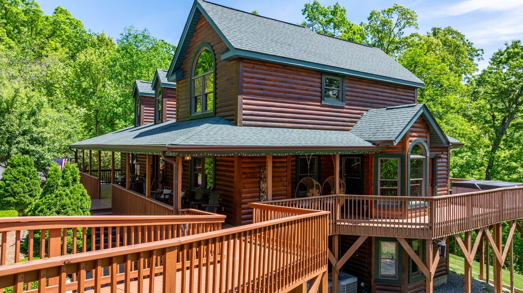 A log cabin with a porch, deck, and multiple windows.
