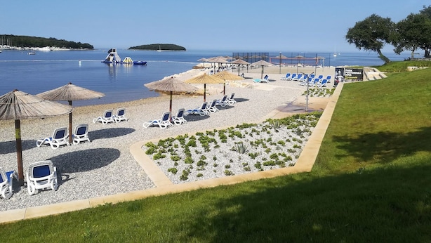 A beach with sun loungers, umbrellas, and a clear view of the sea. - Kleine Wohnung mit schönem Balkon by Interhome (Poreč/Funtana)