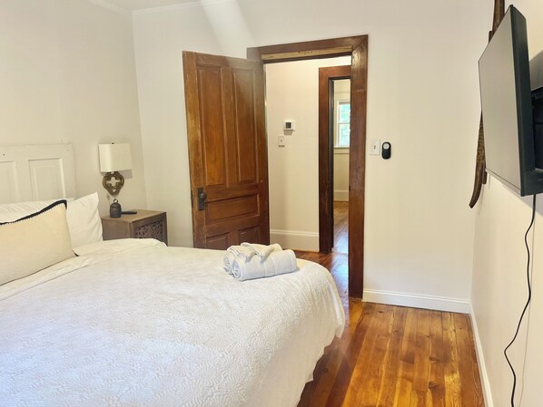 A bedroom with a large bed, wooden door, and a TV mounted on the wall. - The Vintage Vibe- Five Points, sleeps 6, pets ok (Raleigh)