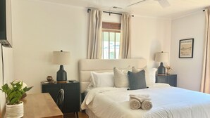 Een hotelkamer met een bed, nachtkastjes, een bureau, een stoel, een potplant en een plafondventilator.
