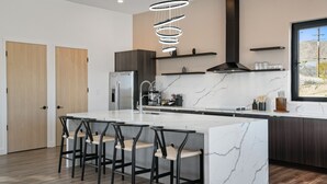 A modern kitchen with a marble island, black bar stools, a stainless steel refrigerator, and a pendant light. - Oasi Espresso|AMAZING mountain views|Cantilevered house w/cowboy pool (Yucca Valley)