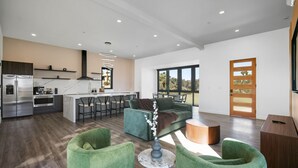 A modern kitchen with a central island, bar stools, and a large window. - Oasi Espresso|AMAZING mountain views|Cantilevered house w/cowboy pool (Yucca Valley)
