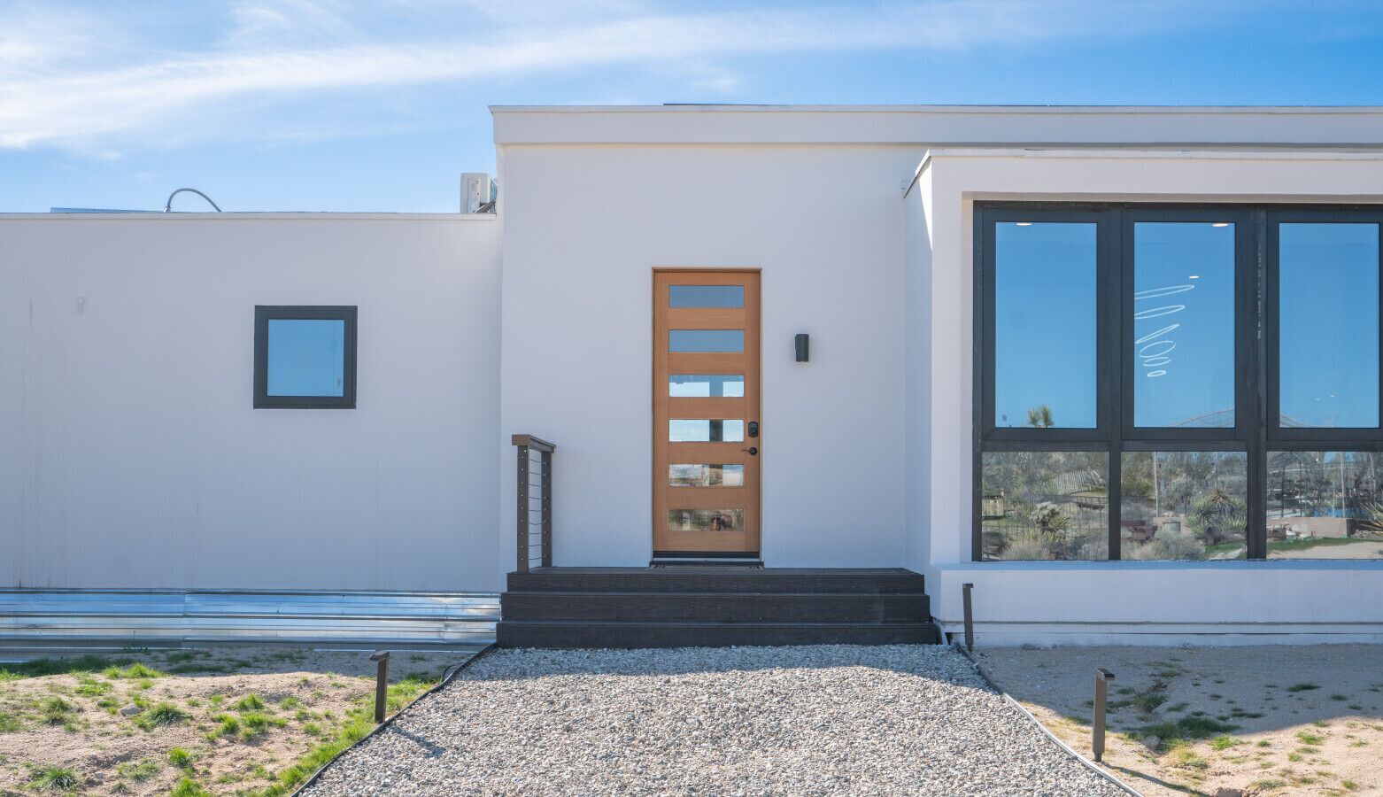 A modern building with a wooden door, large windows, and a gravel pathway leading to the entrance.