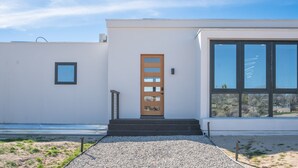 A modern building with a wooden door, large windows, and a gravel pathway leading to the entrance. - Oasi Espresso|AMAZING mountain views|Cantilevered house w/cowboy pool (Yucca Valley)