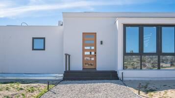 A modern building with a wooden door, large windows, and a gravel pathway leading to the entrance.