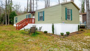 A single-story mobile home with a red staircase, a small patio with two chairs, and a white fence surrounding the property. - 3BR FOREST NEST in Columbus, GA (Columbus)