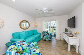 A living room with a teal sofa, a colorful bean bag, a white coffee table, a ceiling fan, and a flat-screen TV. - Siesta Key Luxe w/ Pool, Rooftop & Steps to Beach (Siesta Key)