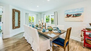 A dining room with a wooden table set for four, white chairs, and a painting of boats on the wall. - Siesta Key Luxe w/ Pool, Rooftop & Steps to Beach (Siesta Key)