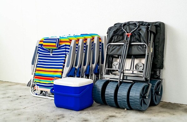 Ein Gepäckwagen mit einer blauen Kühlbox, einem gestreiften Strandtuch und einem schwarzen Koffer.