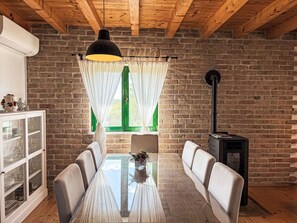 A dining area with a glass table, white chairs, a cabinet with glass doors, a black lamp, and a brick wall. - Anwesen "Steinperle mit beheiztem Schwimmbad" by Interhome (Donje Rastane)