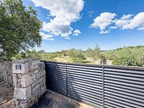 A stone wall with a metal gate, a clear sky, and a distant view of a building with a red roof. - Anwesen "Steinperle mit beheiztem Schwimmbad" by Interhome (Donje Rastane)
