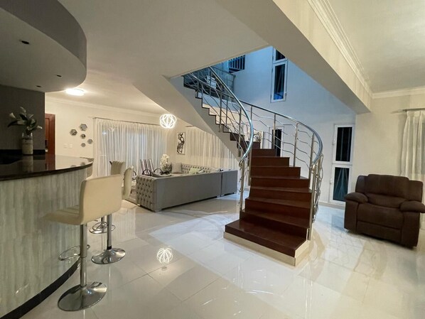 A modern living room with a staircase, a sofa, and a bar area. - Beautiful Villa in Dominican Republic
“Aleimy” (La romana)