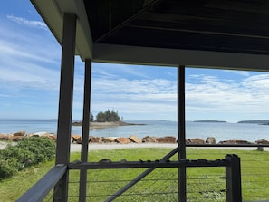 Blick auf die Küste von einer überdachten Fläche mit Geländer, mit einer grünen Wiese im Vordergrund und einer felsigen Küstenlinie.