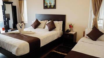 Een hotelkamer met twee bedden, een donker hoofdeinde, een nachtkastje, een ingelijst beeld aan de muur, en een hart-vormige handdoek op het bed.