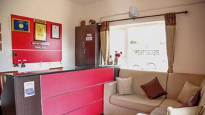 A reception desk with a red and white color scheme, a beige sofa with cushions, and a window with curtains.