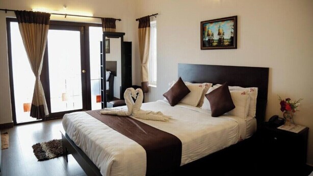 A hotel room with a large bed, a painting on the wall, and a view of the outside through the window.