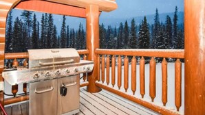 Una terraza de madera con una parrilla incorporada y vistas a un bosque nevado.