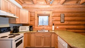 Cocina de cabaña de troncos con gabinetes de madera, una estufa, un microondas y un lavamanos.