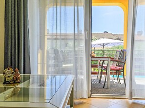 Een kamer met een glazen tafel, een klok en uitzicht op een terras met stoelen en een parasol.