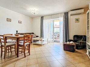 Een woonkamer met een eettafel, stoelen, een bank, een salontafel en een boekenkast.