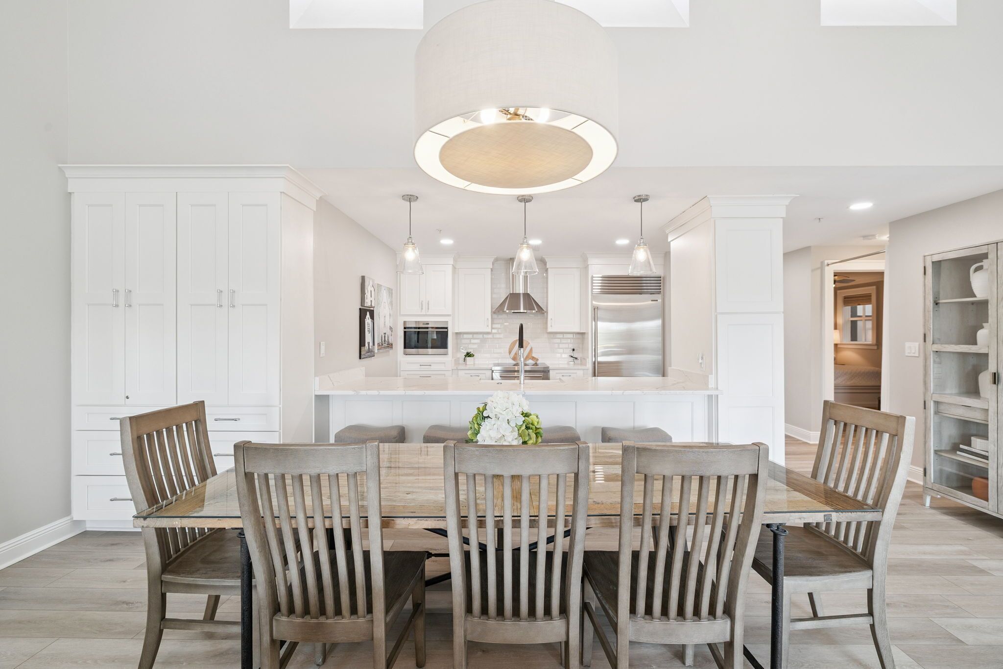 A modern kitchen with white cabinetry, a central island, pendant lighting, and a dining area with wooden chairs.