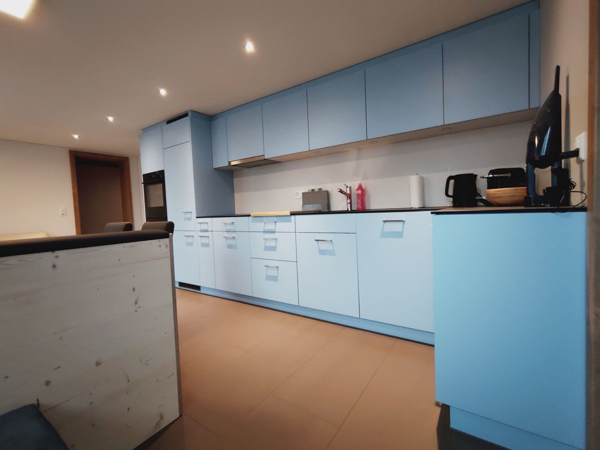 A modern kitchen with light blue cabinets, a black countertop, and various appliances including a coffee maker and a kettle.