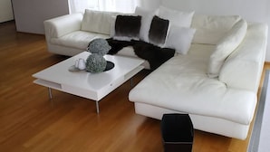 Een moderne woonkamer met een witte modulaire bank, een witte salontafel met decoratieve objecten, en een groot raam met dunne gordijnen.