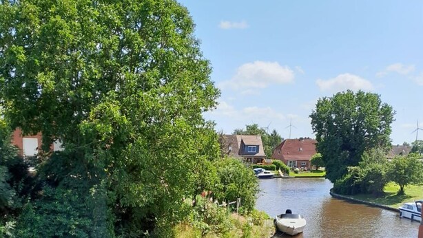 Een rivier met een boot, omringd door groen en huizen.